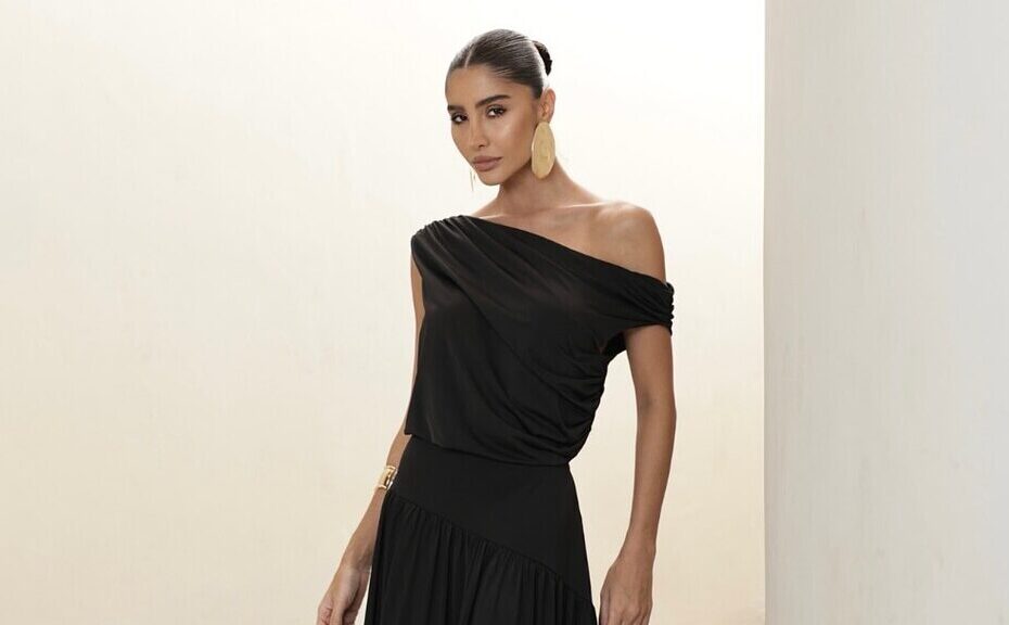Mulher elegante em escadaria minimalista usando vestido preto longo ombro a ombro, acessórios dourados sofisticados, referência inspiradora sobre como escolher vestido longo para ocasiões especiais.