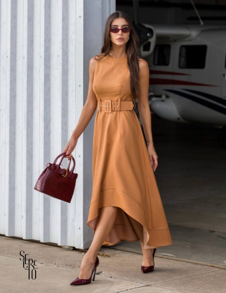 Mulher elegante em vestido para baixinhas: tom camelo, corte mullet, cinto marcando cintura, ideal para compor looks sofisticados com personalidade e estilo.