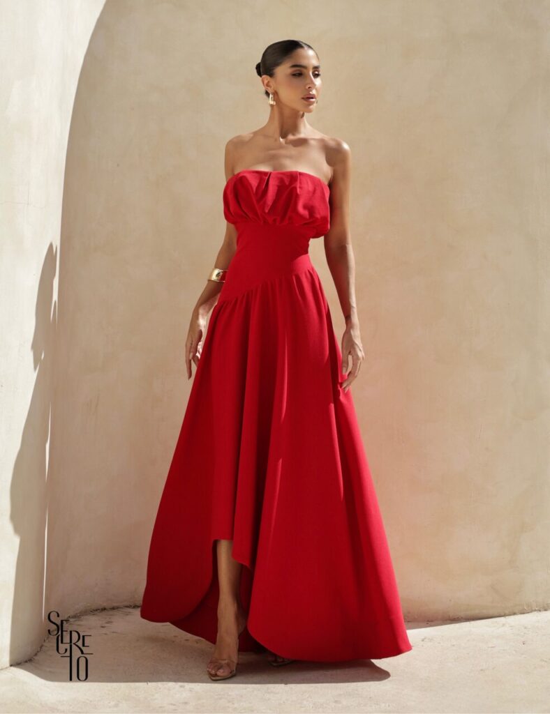 Mulher com vestido vermelho tomara que caia e acessórios dourados, perfeita inspiração de vestidos de convidadas 15 anos para eventos noturnos sofisticados.