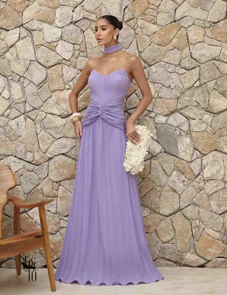 Mulher entre colunas veste vestido de festa com brilho, fenda e drapeado, ilustrando nomes de tecido para vestido de festa glamouroso.