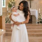 Mulher com bebê em branco em igreja decorada, simbolizando cerimônia religiosa e inspirações de looks para batizado elegantes.