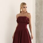 Mulher em vestido para madrinha de casamento burgundy tomara que caia com babados e acessórios dourados.